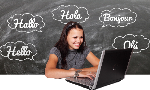 junge Frau mit dunklen langen Haaren sitzt an einem Laptop. Hinter ihr sind an einer Tafel Begrüßungen in verschiedenen Sprachen geschrieben: Hallo, Hello, Ola, Hola, Bonjour